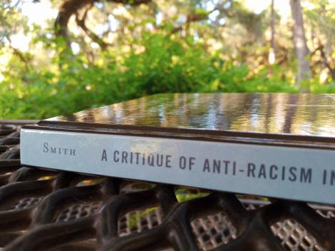 A photo of Erec Smith's book A Critique of Anti-Racism in Rhetoric and Composition, sitting on a picnic table, with green leaves in the background